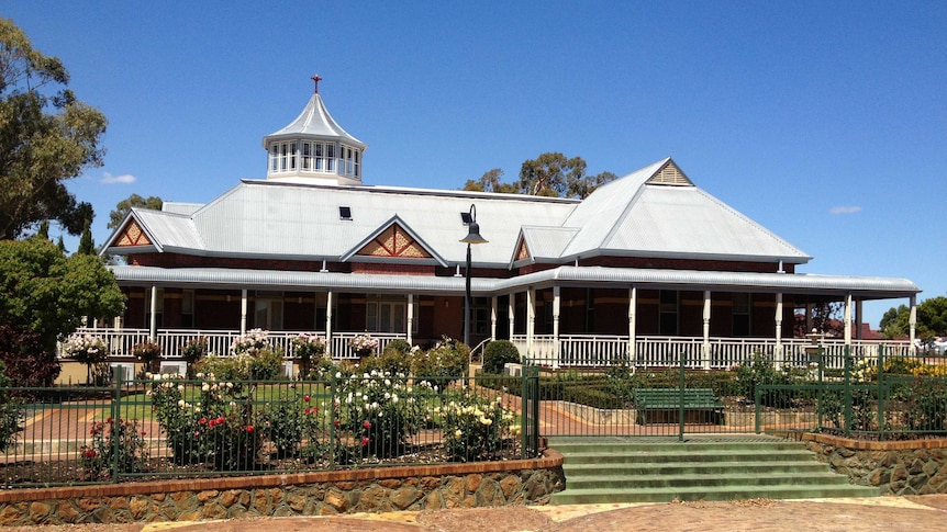 A tin-roofed building with a broad veranda looking out over rose gardens.