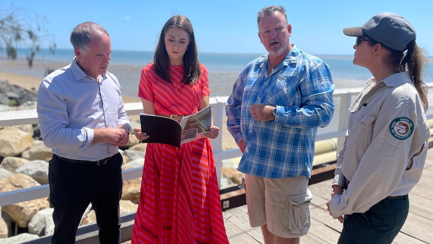 A group of peopled stand on a pier looking at a booklet