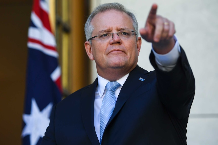Scott Morrison points with his left hand while looking out into a crowd. An Australian flag is behind him.