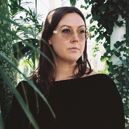 Nadia Reid stands in a tropical garden wearing light tinted sunglasses on the cover of Out Of My Province