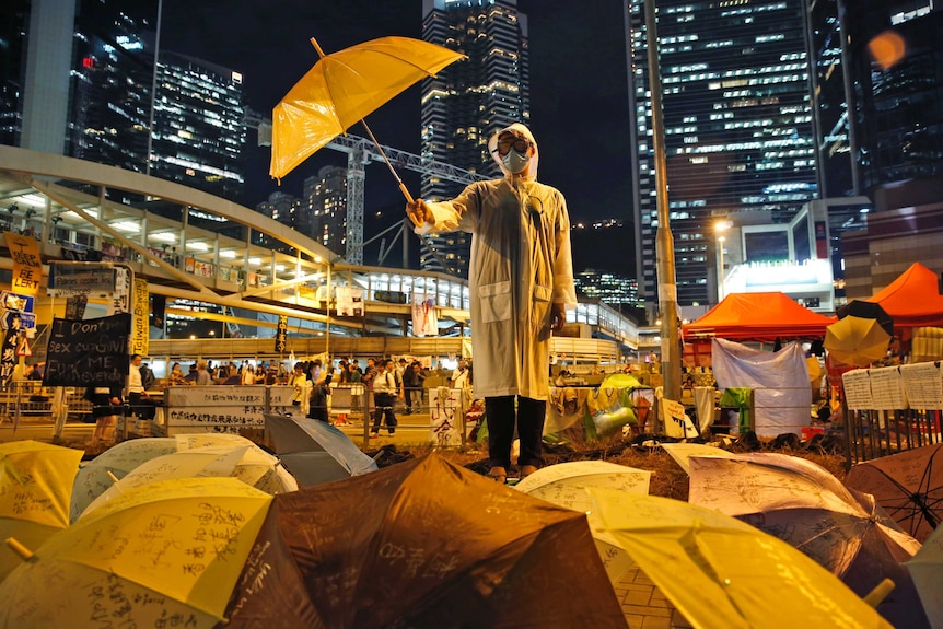 一名穿着黄色雨衣，举着黄色雨伞的男子站在路旁，身边都是黄色雨伞