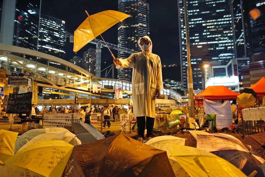 A Hong Kong protester wears a face mask and holds an umbrella defiantly in front of high-rise buildings