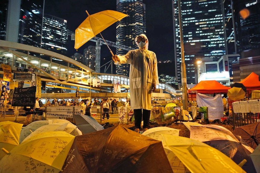 A Hong Kong protester wears a face mask and holds an umbrella defiantly in front of high-rise buildings