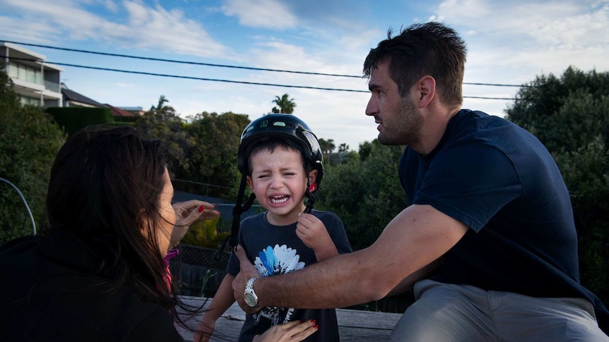 Two parents crouch in front of a child who is crying.