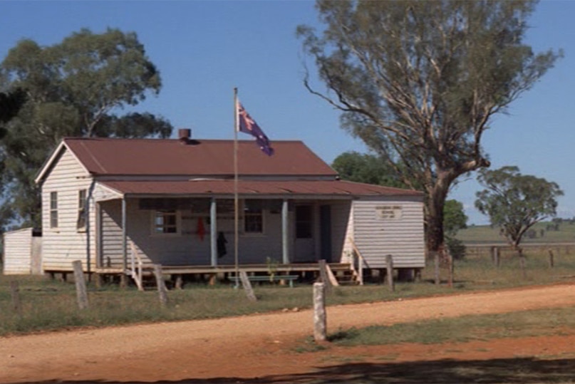 An old weatherboard schoolhouse with a flag pole out the front.