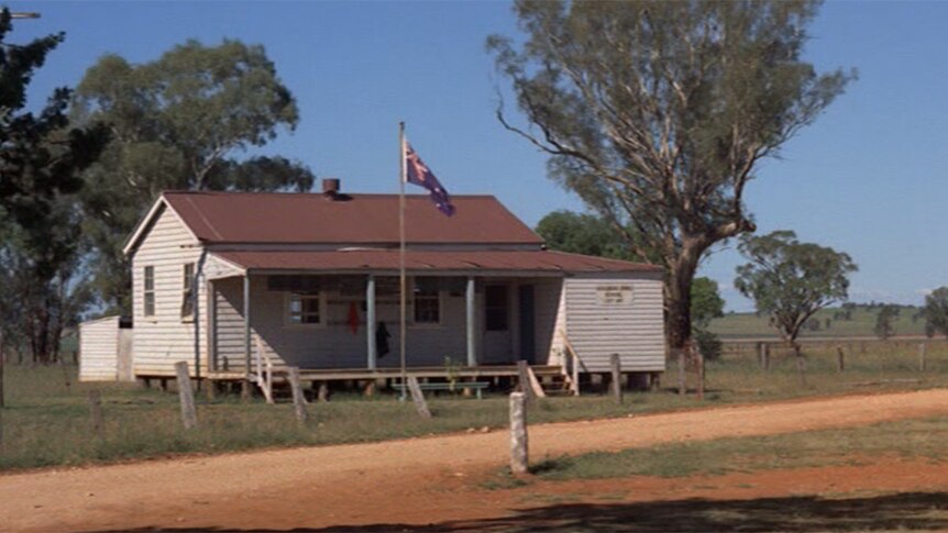 An old weatherboard schoolhouse with a flag pole out the front.