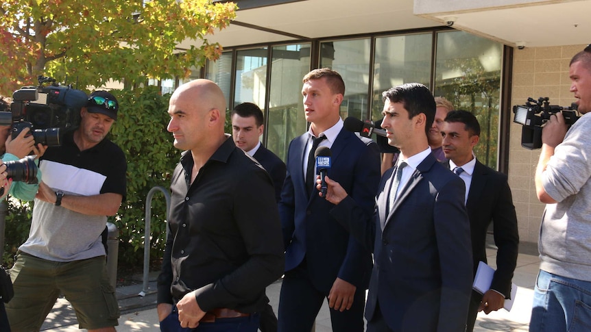 Jack Wighton, in a suit, walks in the middle of a press pack.