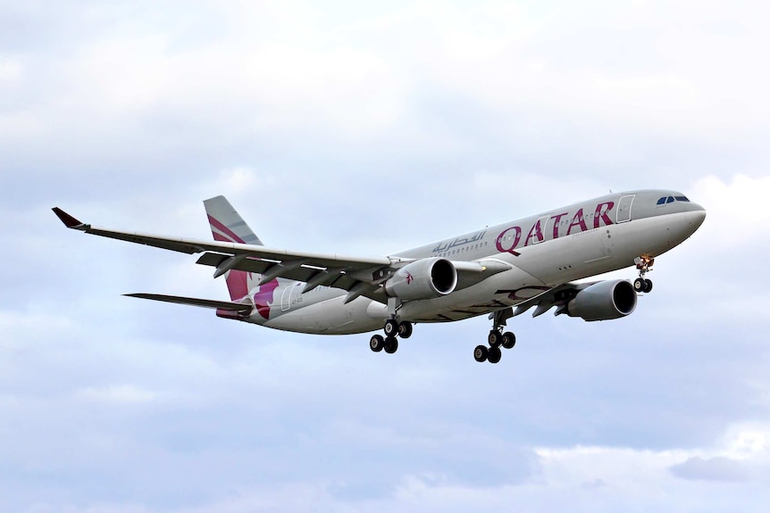 A grey plane with Qatar written in red soars against a blue sky.