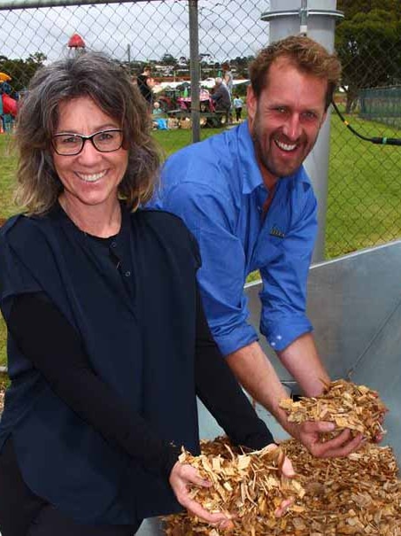 A man and woman hold up piles of woodchips at a local park