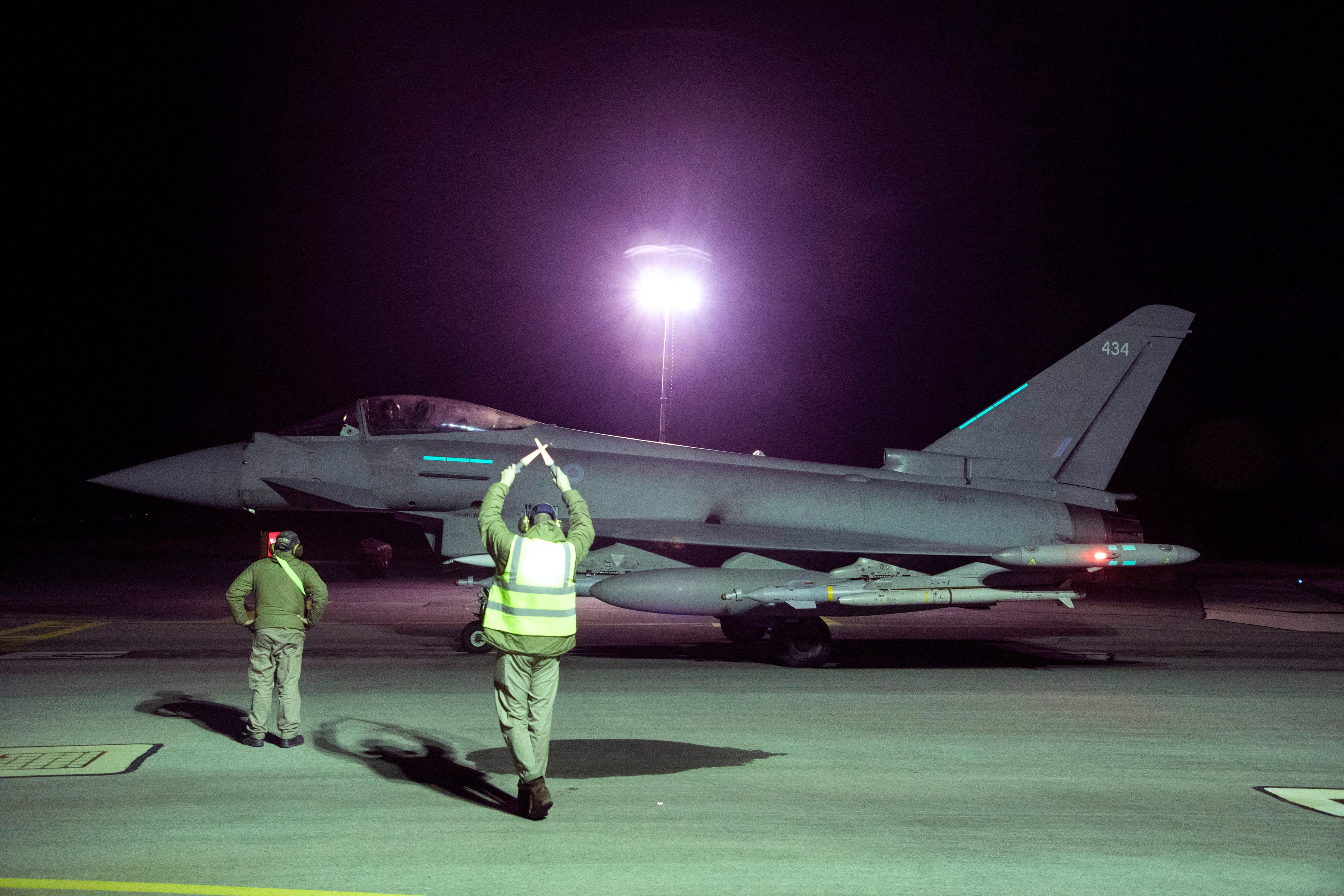 A traffic controlled holds hands above his head with light sticks in front of RAF jet.