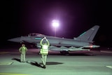 A traffic controlled holds hands above his head with light sticks in front of RAF jet.