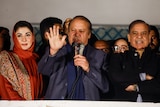 Nawaz Sharif speaks with a microphone flanked by his daughter and a former prime minister.