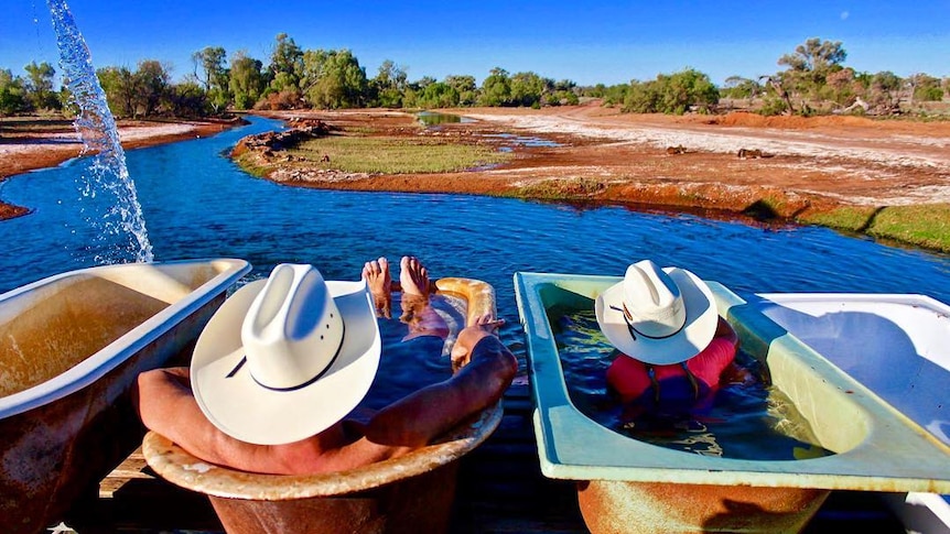 Two people take an outdoor bath beside a waterway in western Queensland.