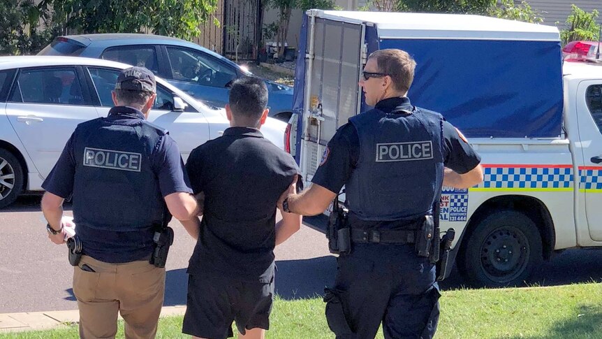 NT Police walk a man out to a paddy wagon after a fraud arrest.