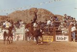 Man riding a horse at a rodeo in front of cheering crowd in the 1970s-1980s