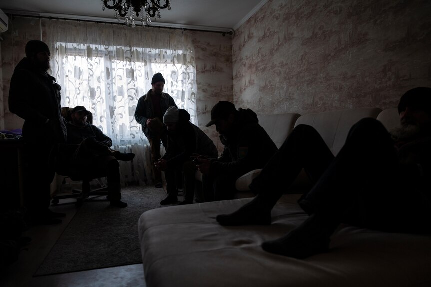 Eight men huddle in darkness in a spare bedroom