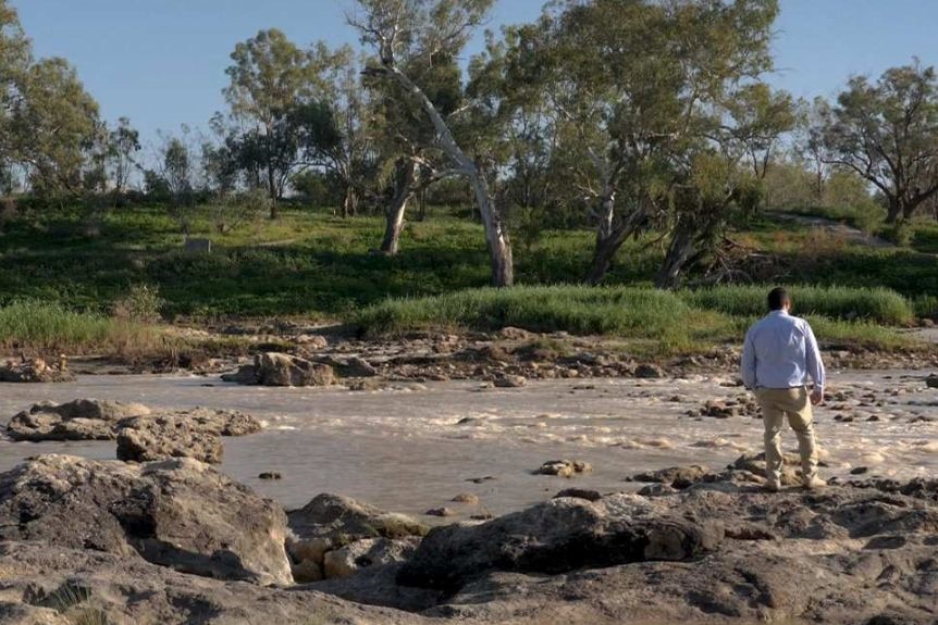 A man stands by the Brewarrina Fish Traps, which is a rock formation in the river.