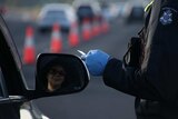 A driver's face in the side mirror as a gloved police officer's hand checks a driver's licence.