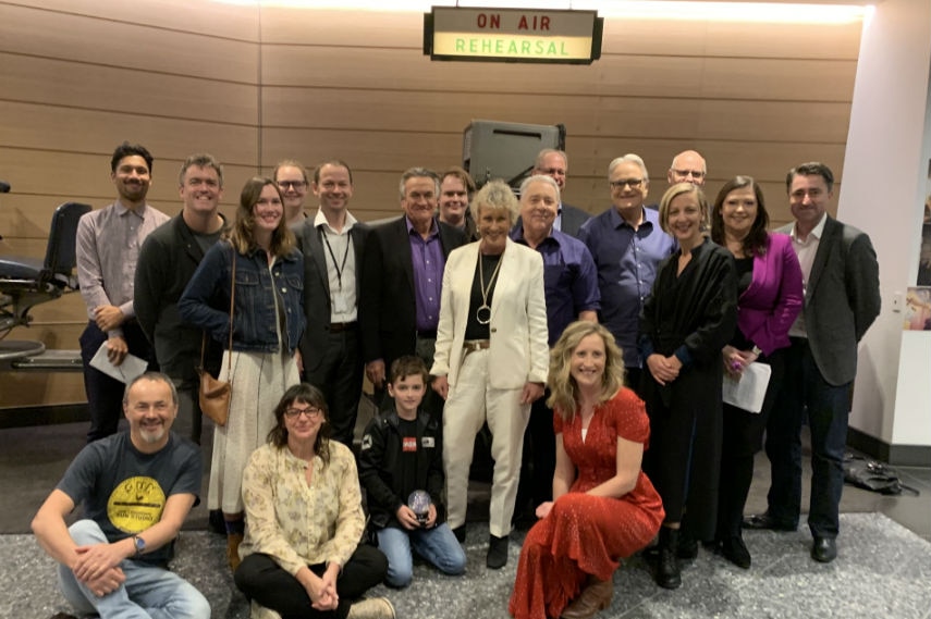 Cassidy with large group of people posing in front of on air sign.