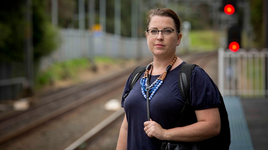 Julia Gilchrist stands on a train platform for railway tracks extending into the distance.