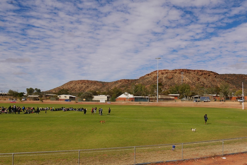 People on a green footy oval in Santa Teresa, with houses and a mountain range in the backdrop. 