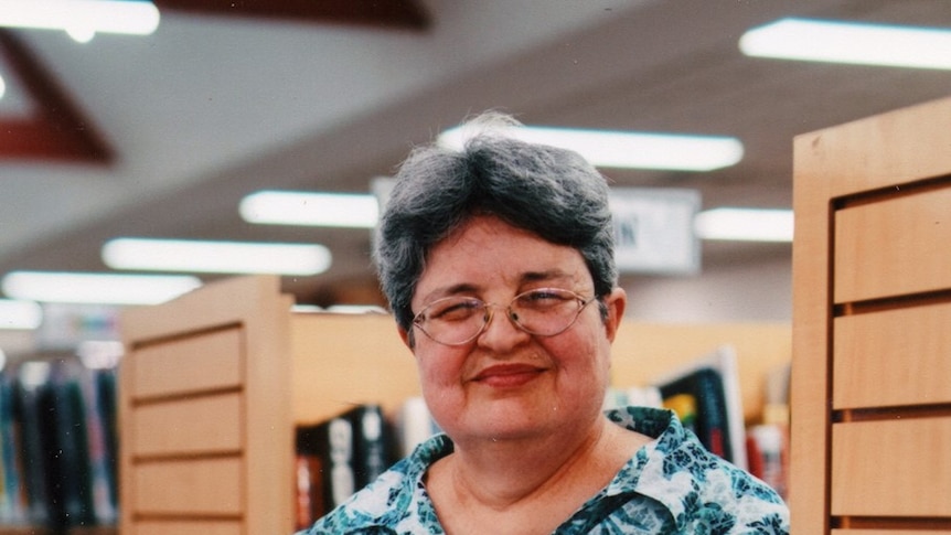 Juanita leaning against a bookcase, holding a book