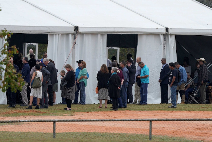 People stand outside an erected marquee listening to a church service.