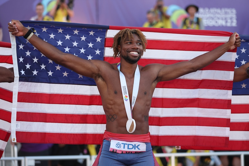 A male American athlete holds the US flag behind his head as he celebrates winning world championships gold medal.