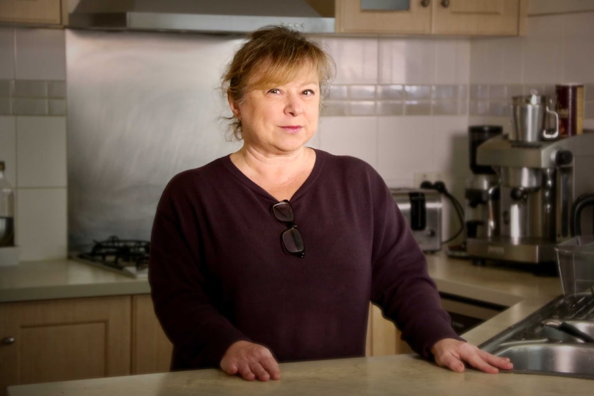 A woman stands at the bench in her kitchen.