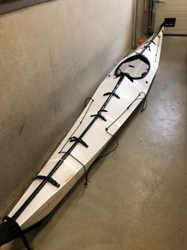 A white kayak sit in on a concrete floor in what looks like a garage or storage container.