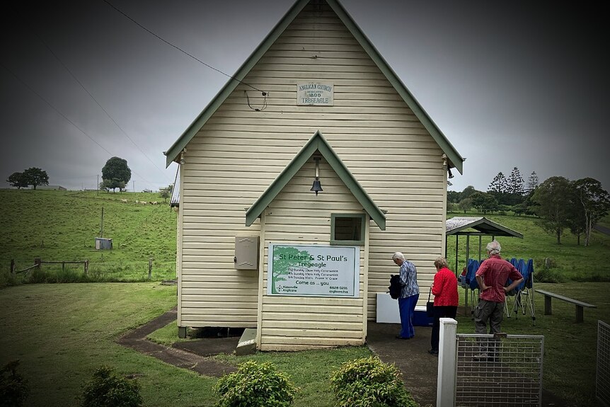 three people entering a church, surrounded by green paddocks