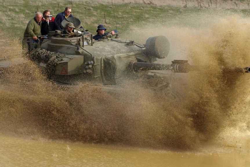 Men driving in military vehicles through a paddock.