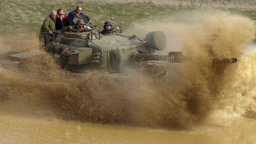 Men driving in military vehicles through a paddock.