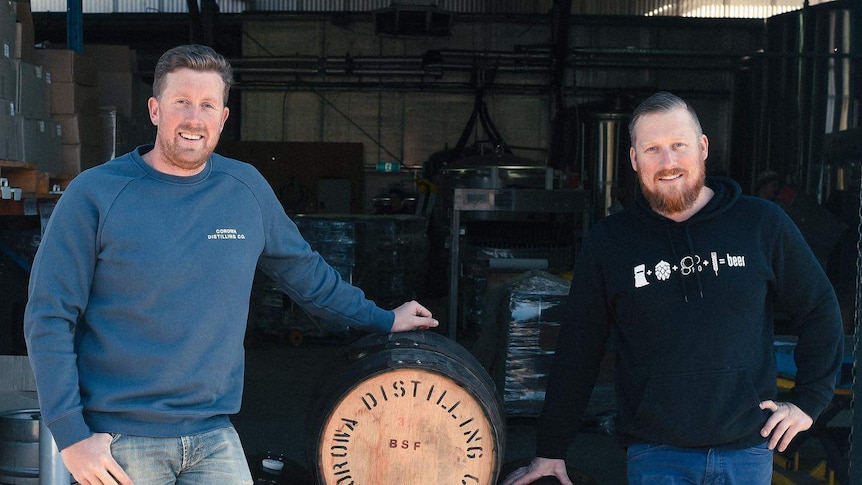 Two men stand next to whiskey barrels