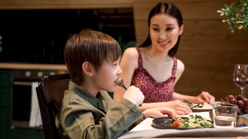 A Young Boy Eating Vegetable Salad watched by his mother at the dinner table