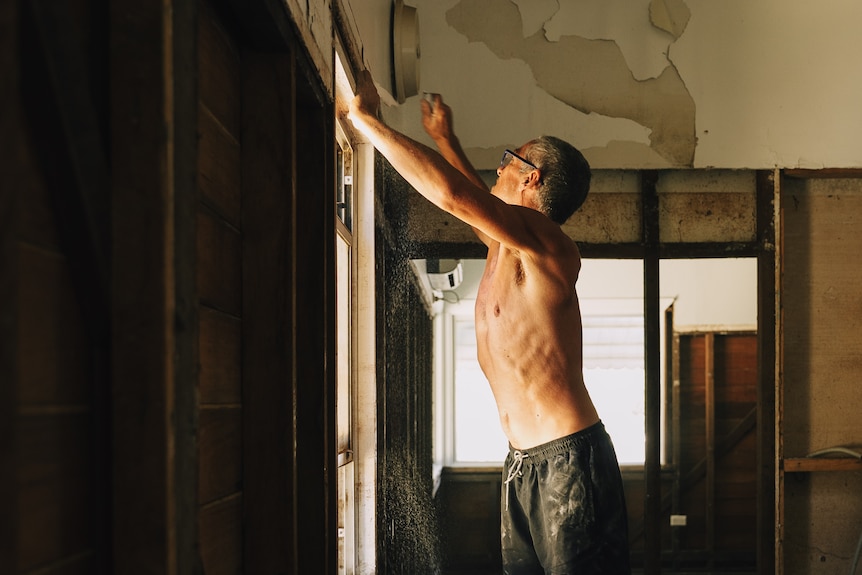 A shirtless man ripping wall from a timber frame
