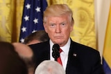 US President Donald Trump standing at a podium in front of reporters