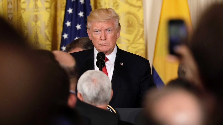 US President Donald Trump standing at a podium in front of reporters