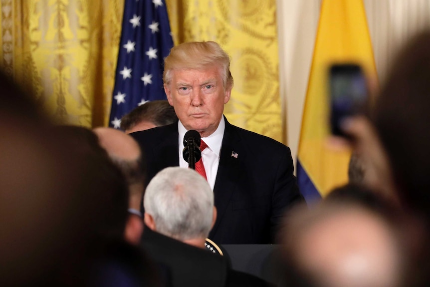 US President Donald Trump standing at a podium in front of reporters