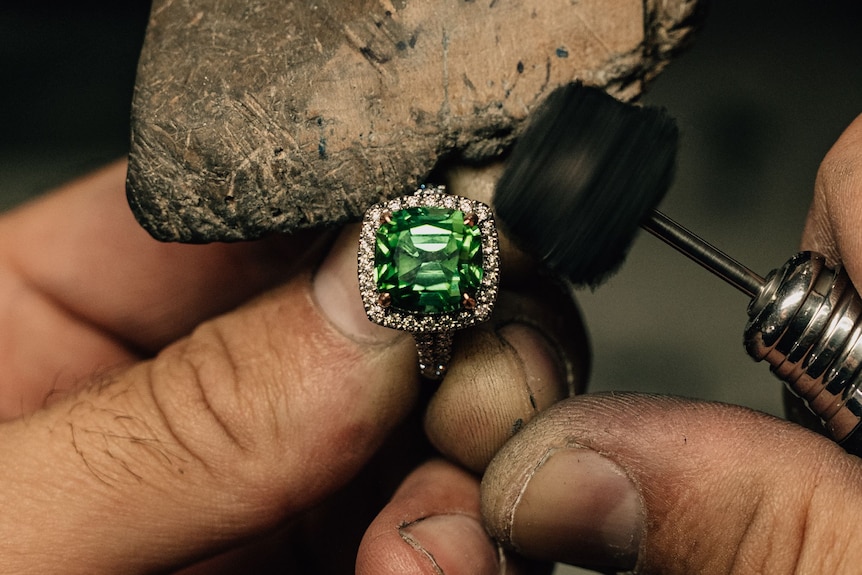A large green gemstone held in hands against a tool.