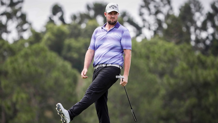 Marc Leishman raises one leg as he watches a putt.