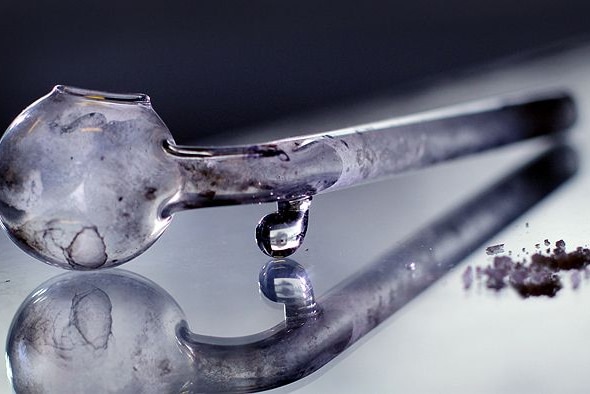 A glass pipe with shards of crystal methamphetamine on a desktop.