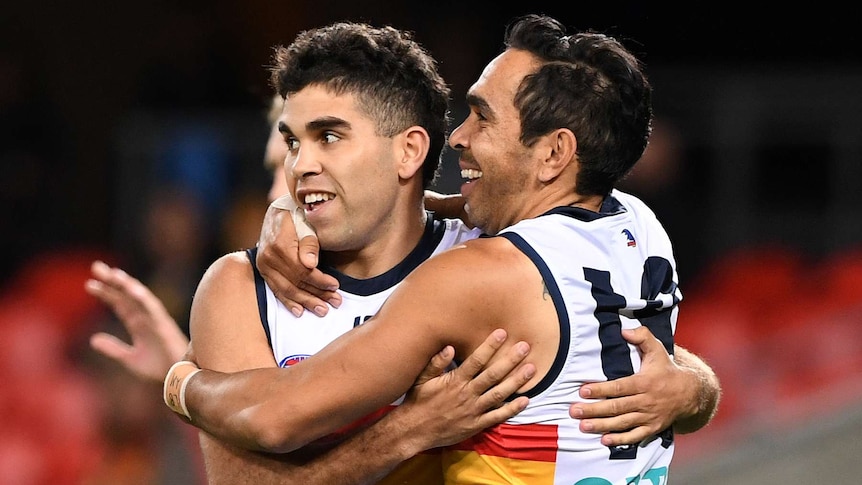 A male AFL player smiles as he hugs a teammate after he kicked a goal.