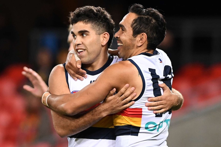 A male AFL player smiles as he hugs a teammate after he kicked a goal.