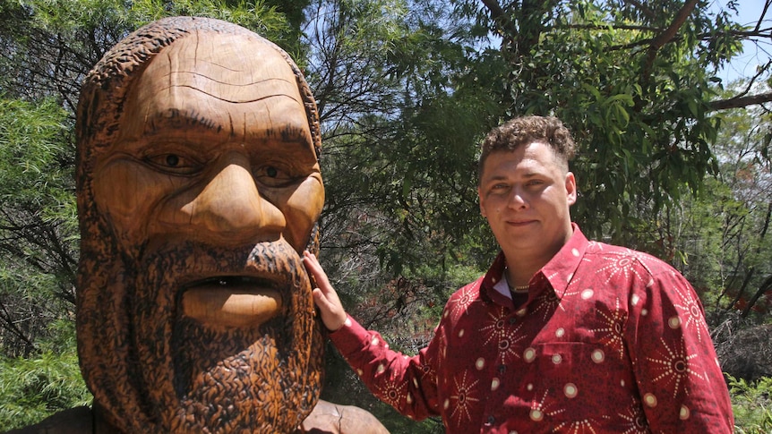 Aboriginal man Max Dillion with large wooden statue of Aboriginal Dreaming God Jabreen which has an open mouth.