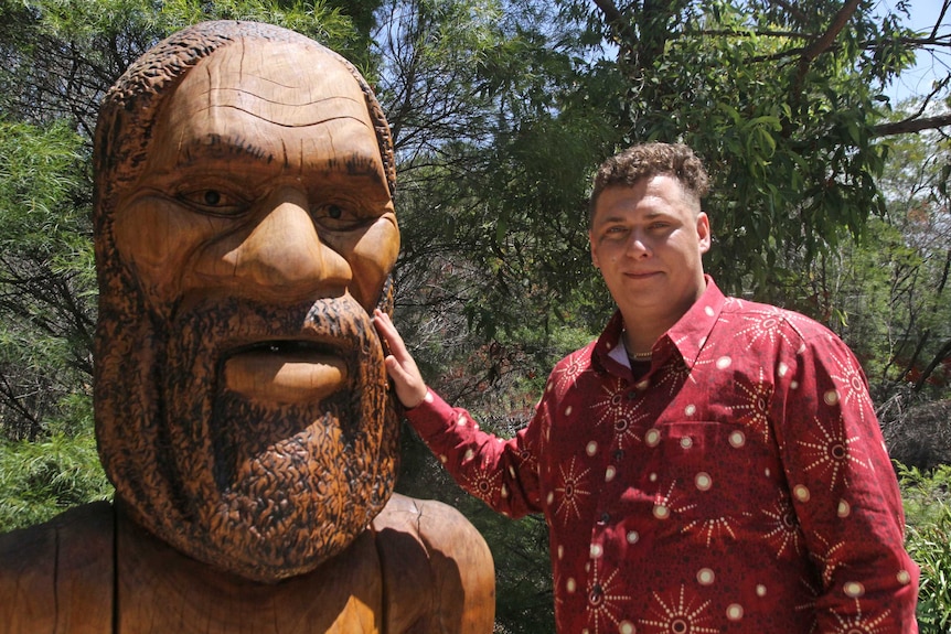 Aboriginal man Max Dillion with large wooden statue of Aboriginal Dreaming God Jabreen which has an open mouth.