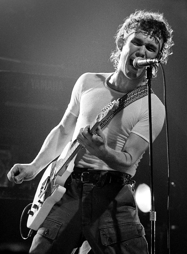 A man screams into the microphone while playing guitar