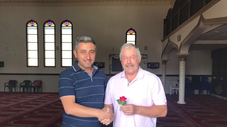 Two men shake hands inside a mosque.
