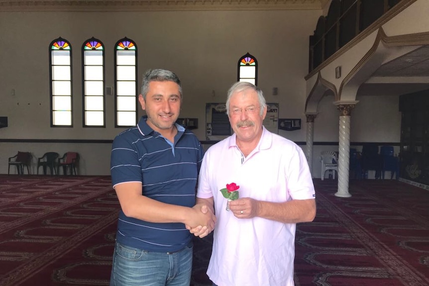 Two men shake hands inside a mosque.