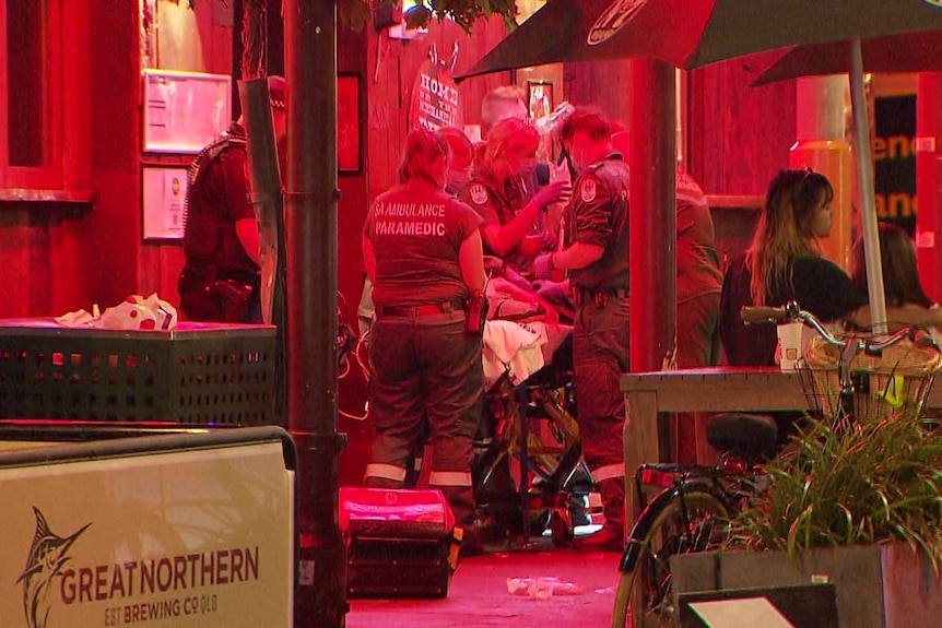 Paramedics attending to a person on an ambulance stretcher outside a bar with red lights